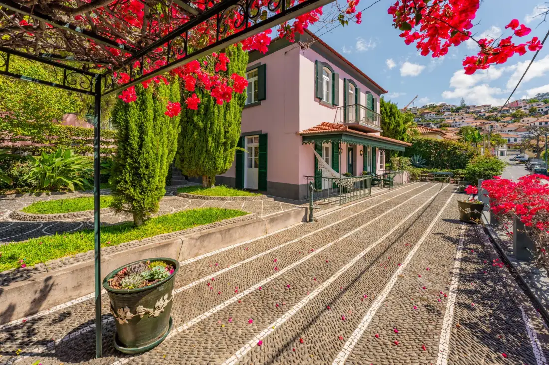 Una casa rosa junto a un patio estampado, con enredaderas floridas por encima.