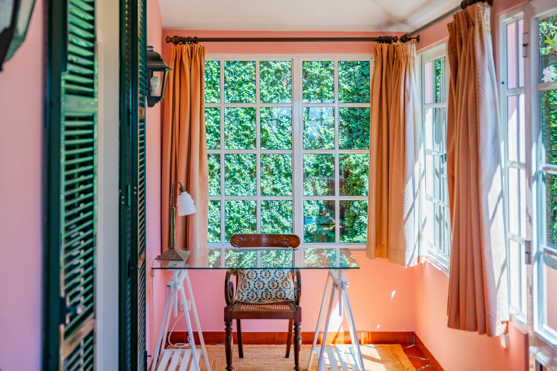 Una habitación luminosa con un escritorio pequeño y una silla junto a grandes ventanas.