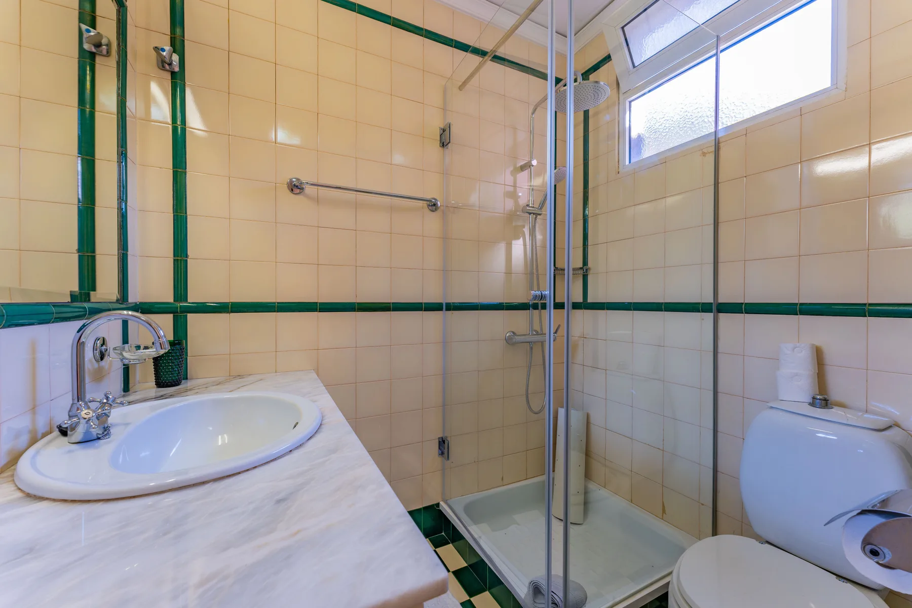 Baño con azulejos, lavabo y ducha con mampara de vidrio.