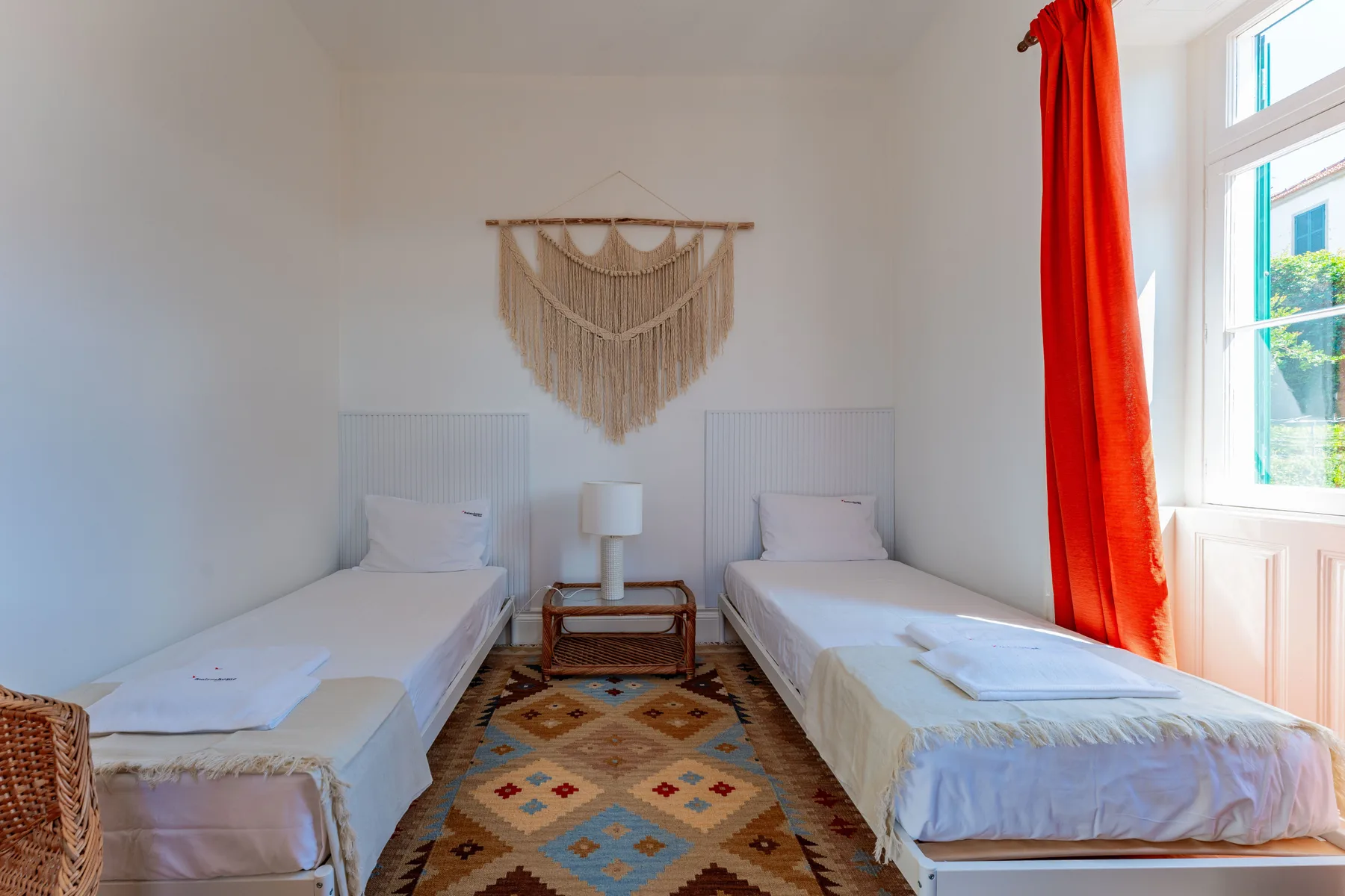 Un dormitorio con dos camas individuales, un tapiz tejido y una ventana luminosa.