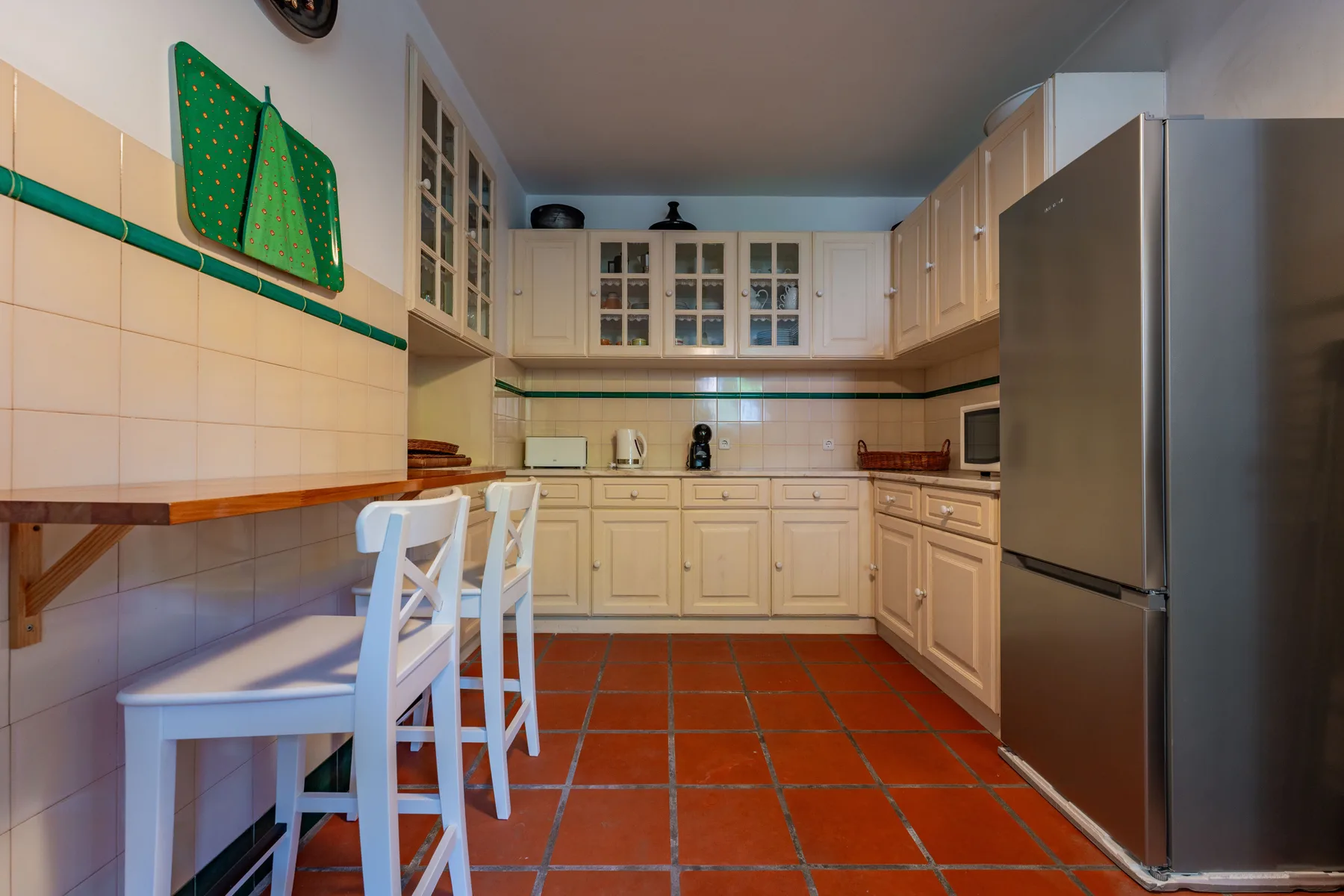 Una cocina con azulejos, armarios claros, una encimera y un refrigerador.
