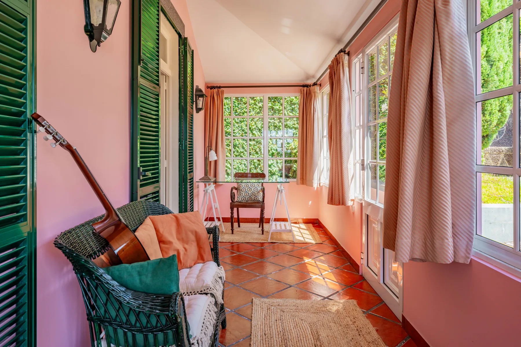 Una sala de estar luminosa con contraventanas verdes, grandes ventanas y asientos.