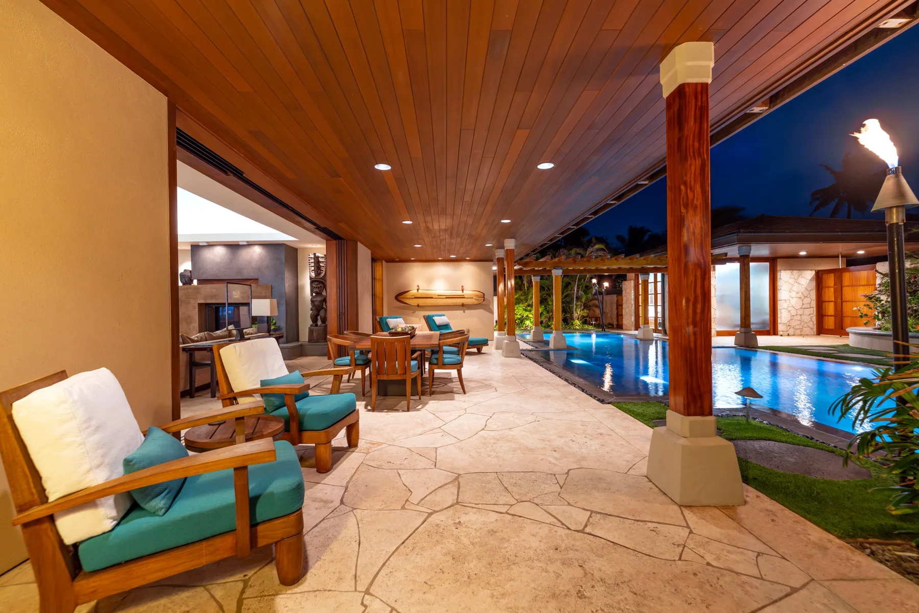 Una sala cubierta junto a la piscina, con asientos al lado de una piscina iluminada.