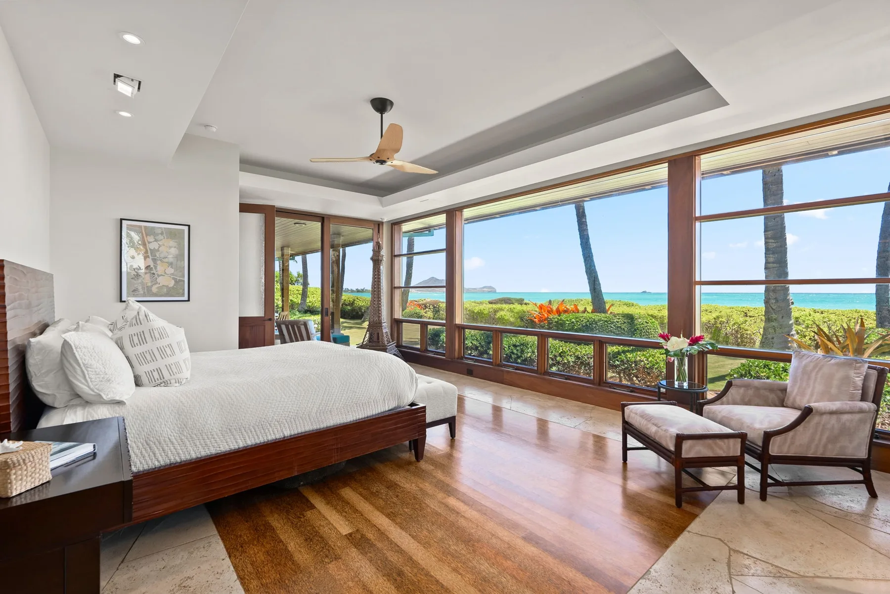Un dormitorio con cama y asientos junto a amplios ventanales con vista al mar.