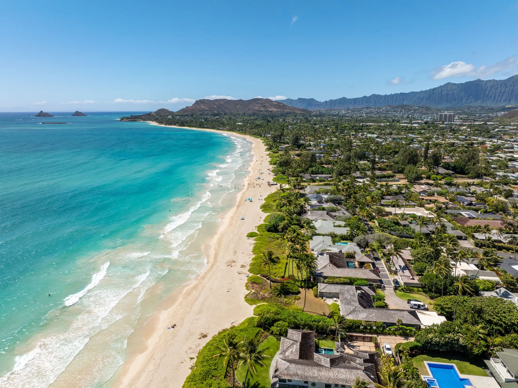 Vista aérea de una costa arenosa junto a aguas turquesas y un barrio residencial.