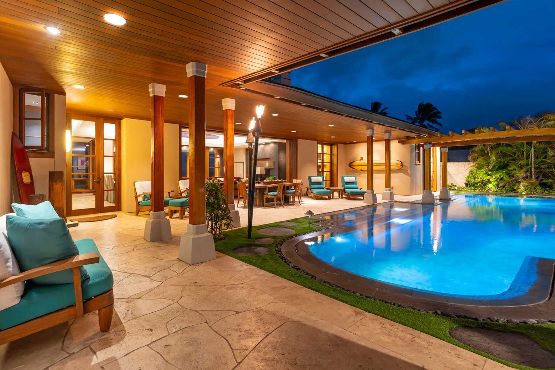 Un patio cubierto con asientos da a una piscina iluminada al anochecer.