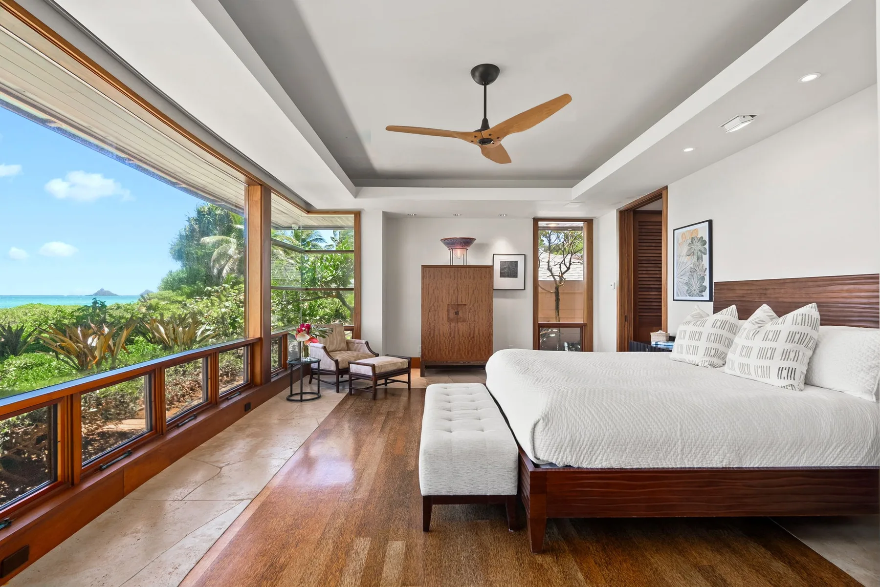 Un dormitorio con una cama grande junto a amplias ventanas con vistas a árboles verdes.