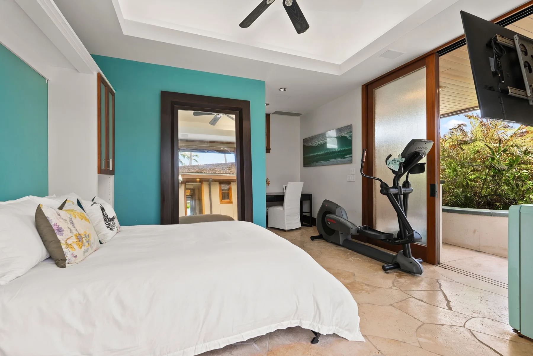 Un dormitorio con una cama y equipo de ejercicio junto a puertas de vidrio que dan a un balcón.