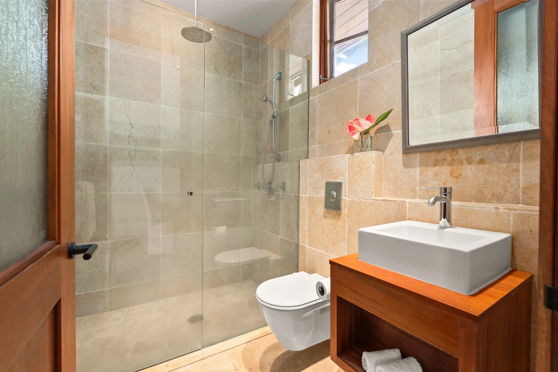 Un baño de azulejos con ducha de vidrio, inodoro y lavabo sobre un mueble.