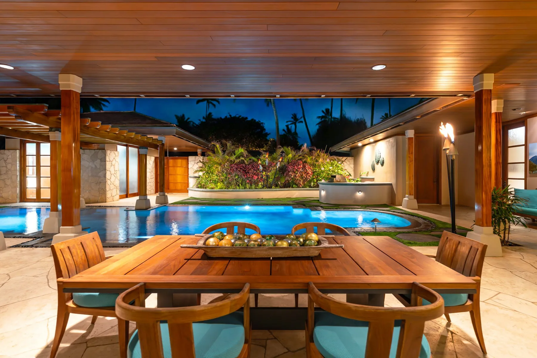 Una zona de comedor exterior cubierta da a una piscina y un jardín.