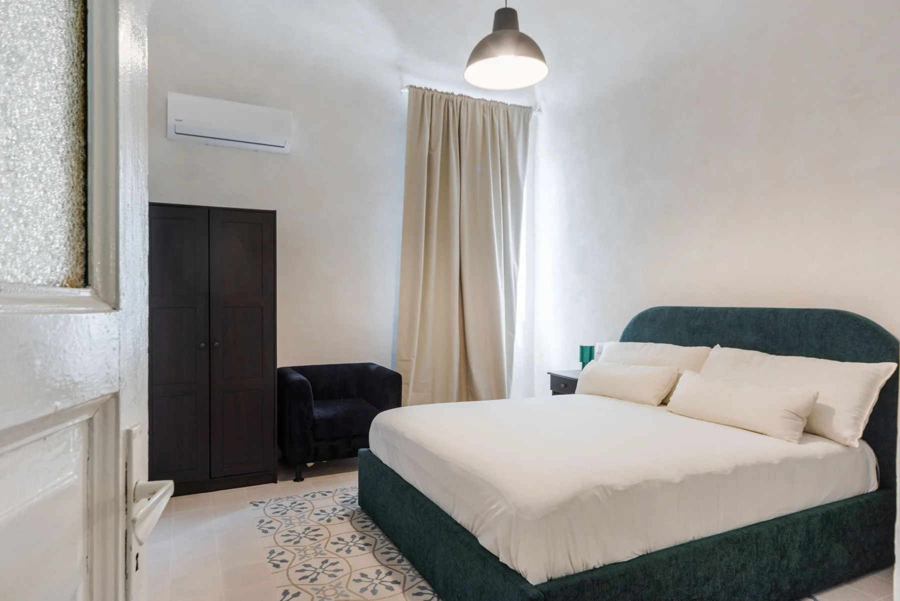 Un dormitorio con una cama grande, cabecero tapizado oscuro y ventana con cortinas.