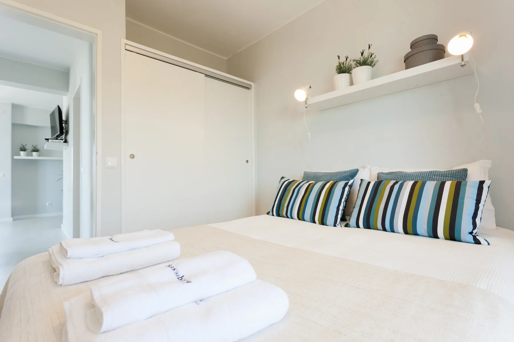 Un dormitorio con cojines a rayas y toallas dobladas sobre la cama.