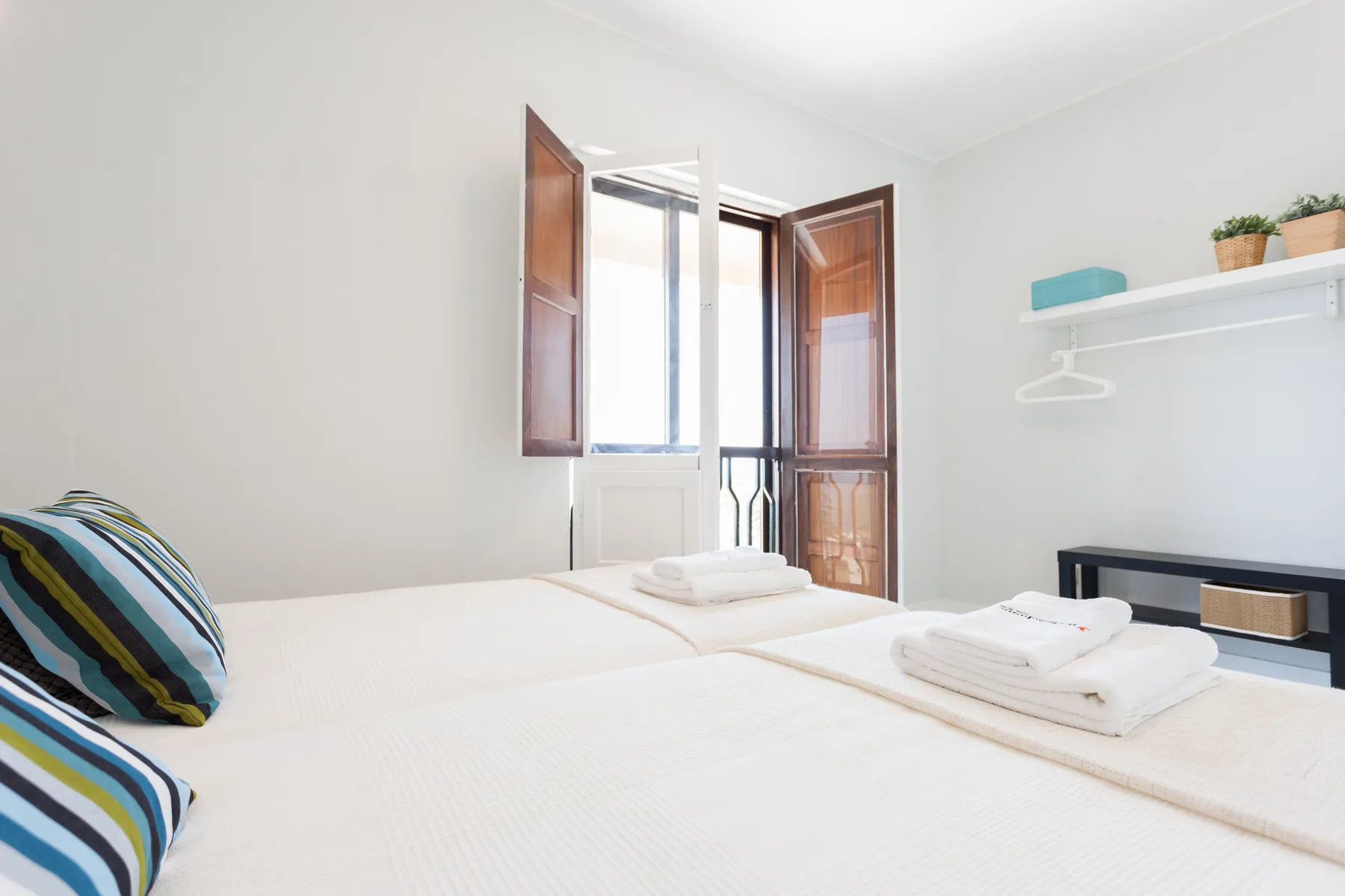 Dormitorio con dos camas, toallas dobladas y contraventanas de madera abiertas.