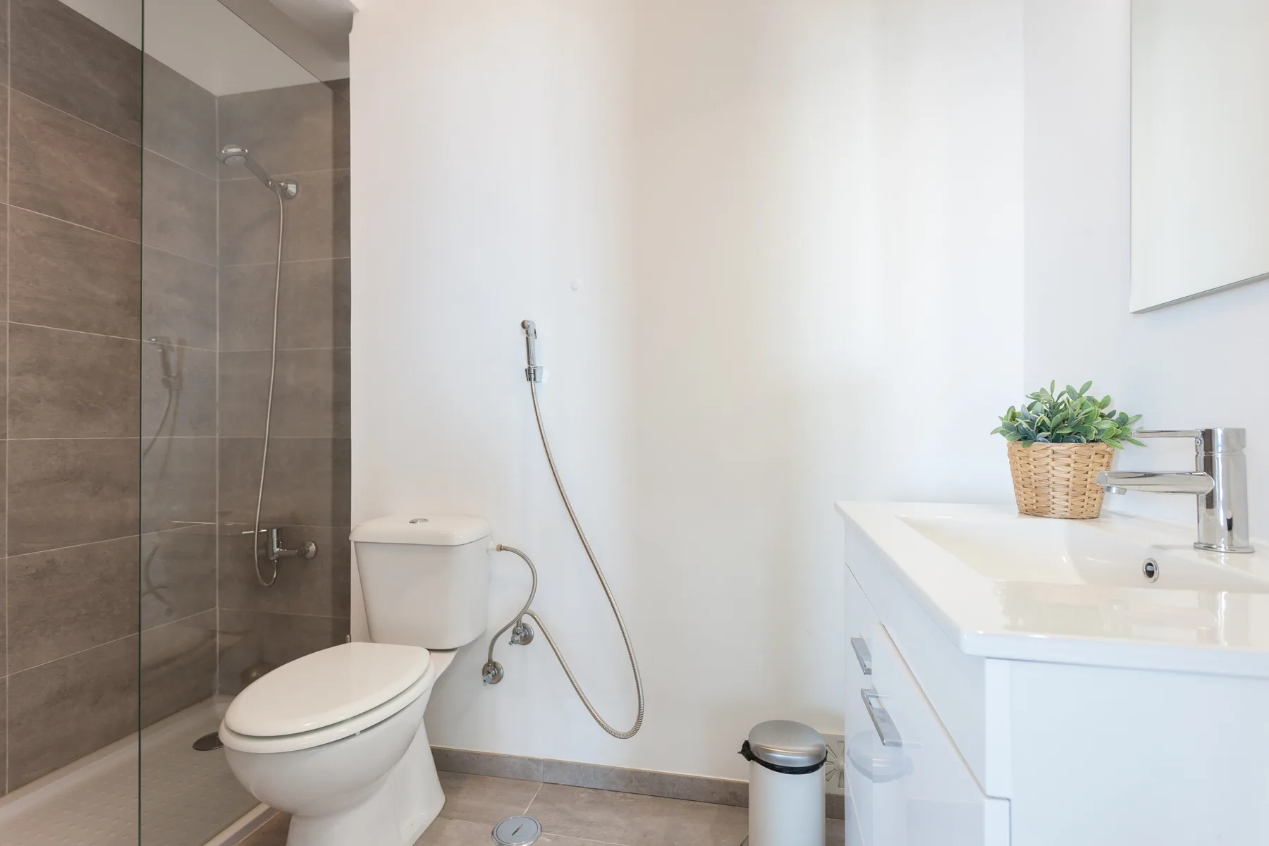 Un baño luminoso con inodoro, ducha y mueble de lavabo blanco.