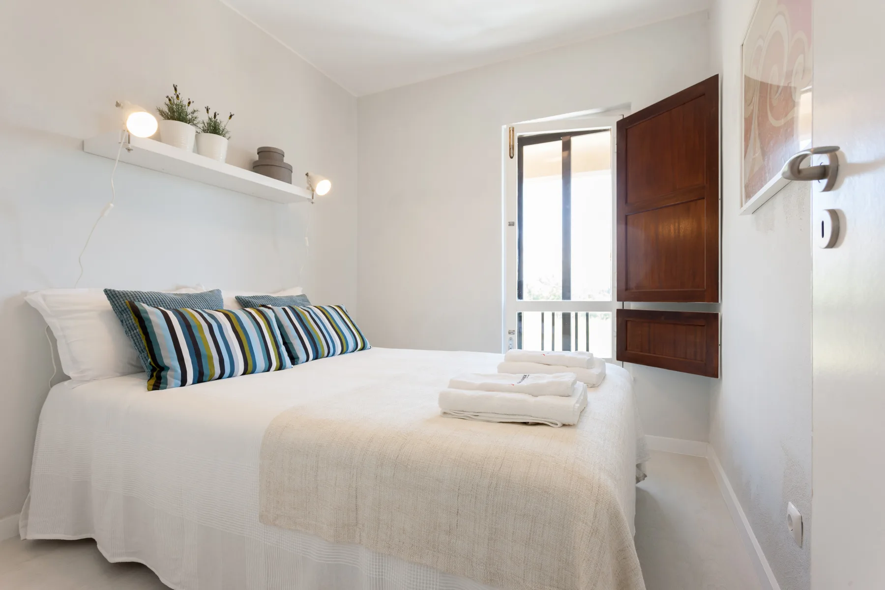 Un dormitorio luminoso con una cama tendida y cojines decorativos a rayas.