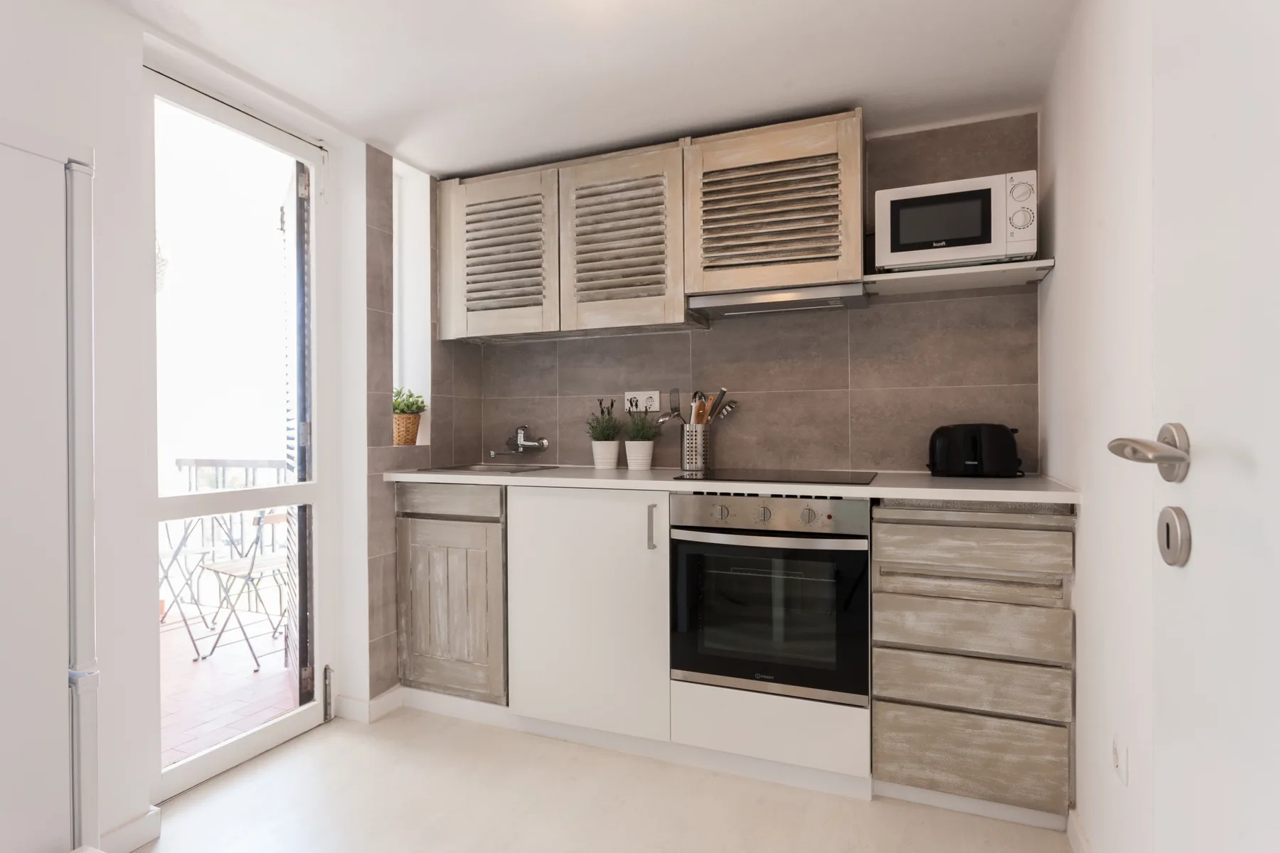 Una cocina compacta con horno, microondas y una puerta de vidrio que da a un balcón.