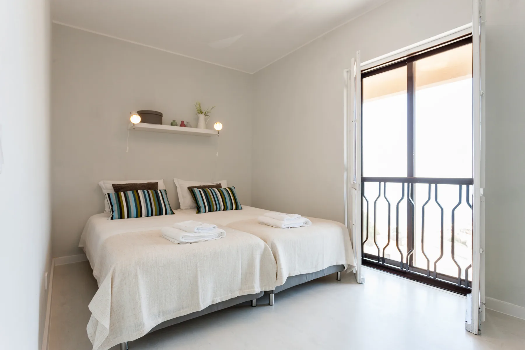 Un dormitorio luminoso con dos camas junto a una puerta de cristal al balcón.