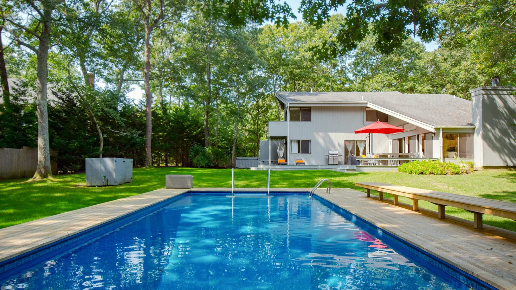 An outdoor swimming pool beside a modern house, surrounded by trees.