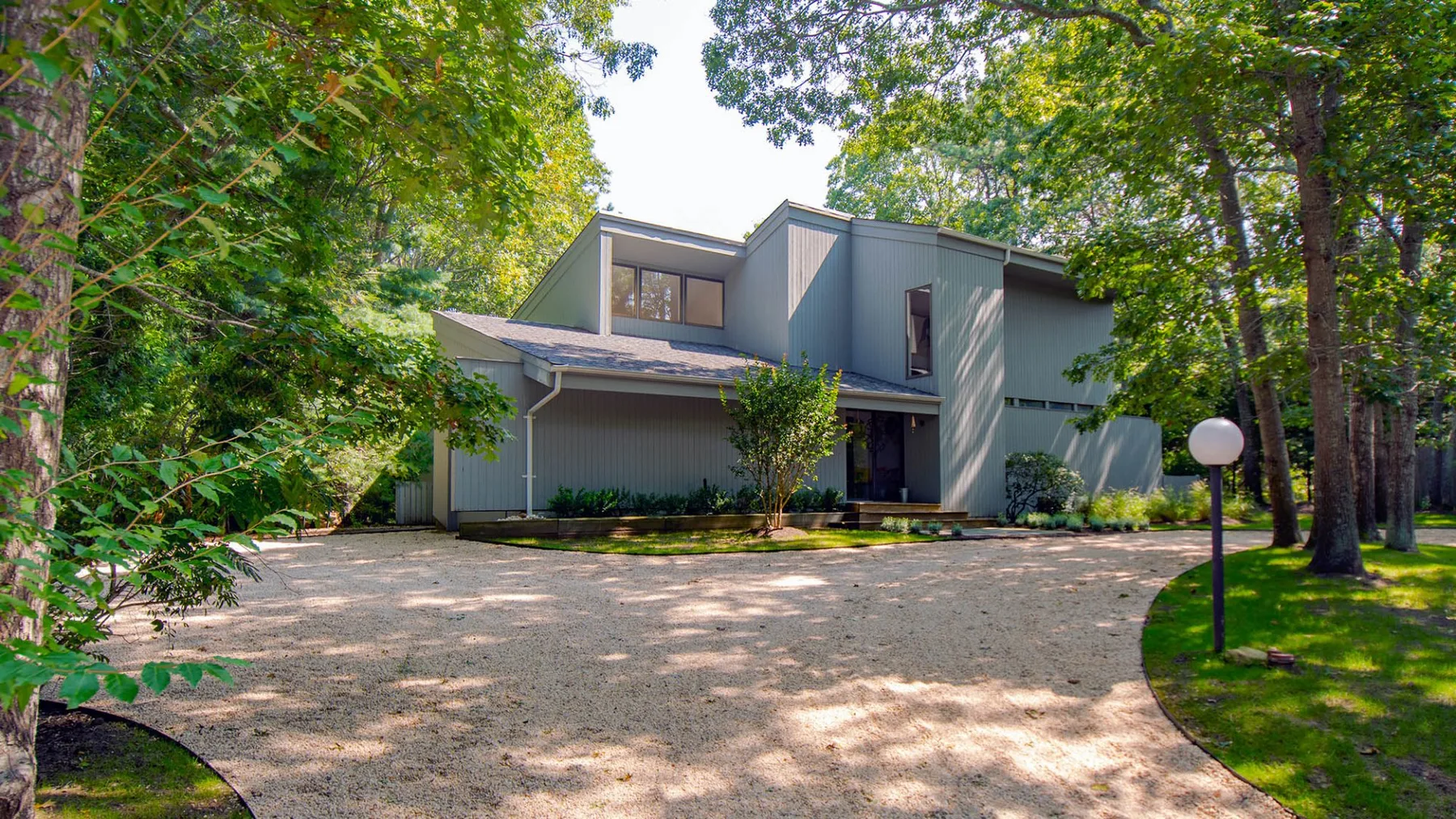 A modern house stands among trees beside a broad paved driveway.