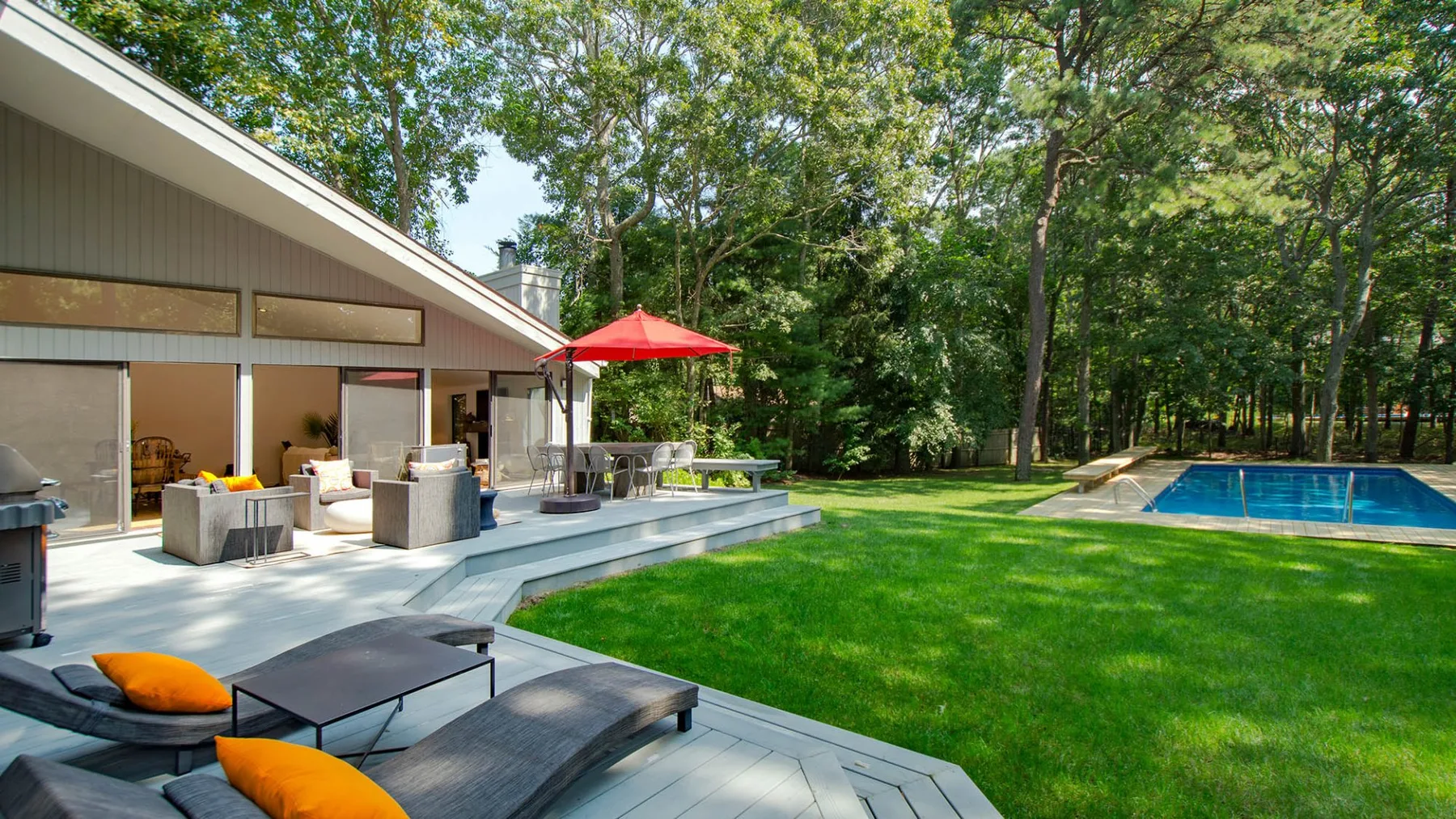 A modern house opens onto a patio beside a green lawn and swimming pool.