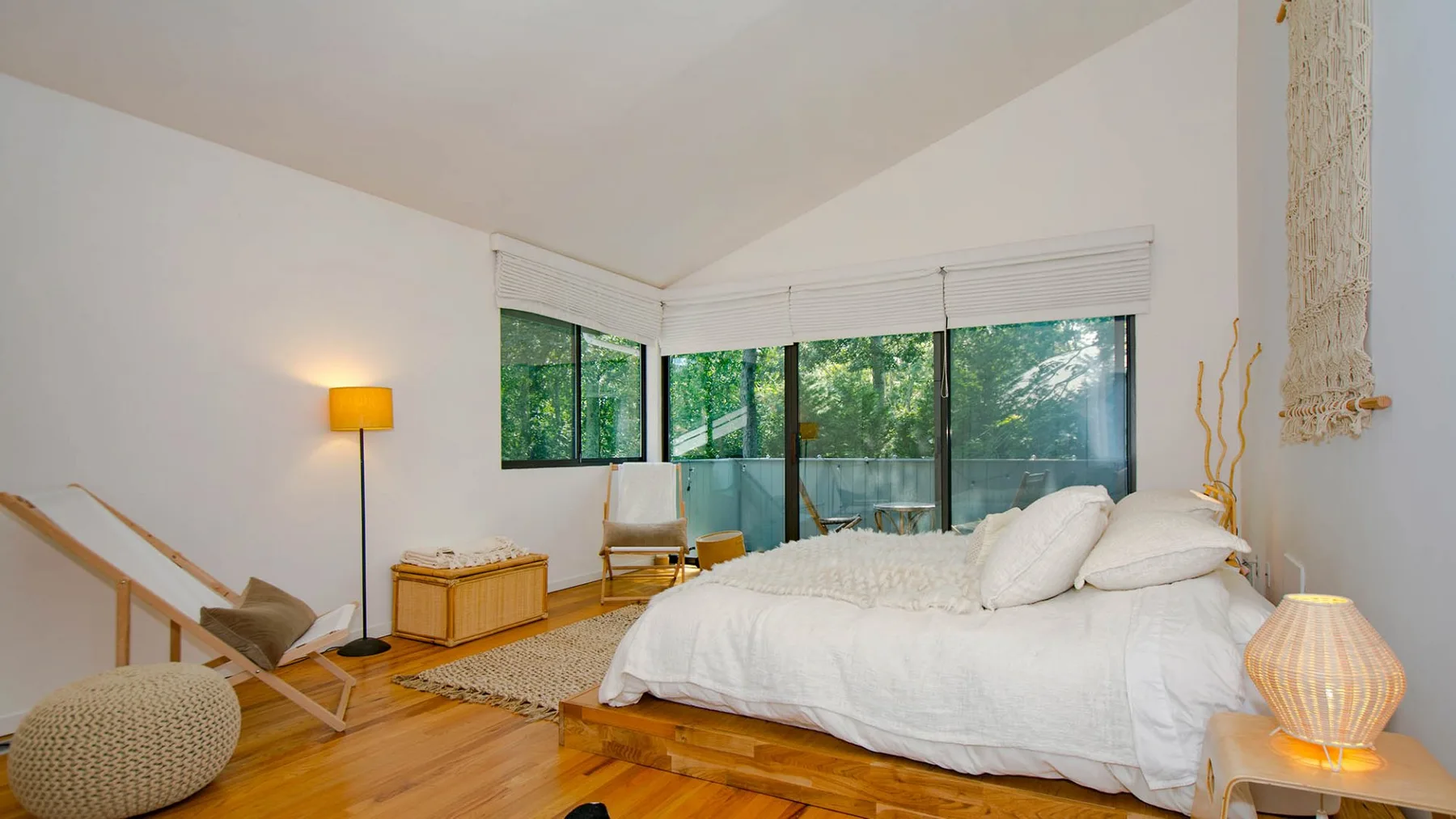 A bright bedroom with a white bed, corner windows, and warm wood flooring.