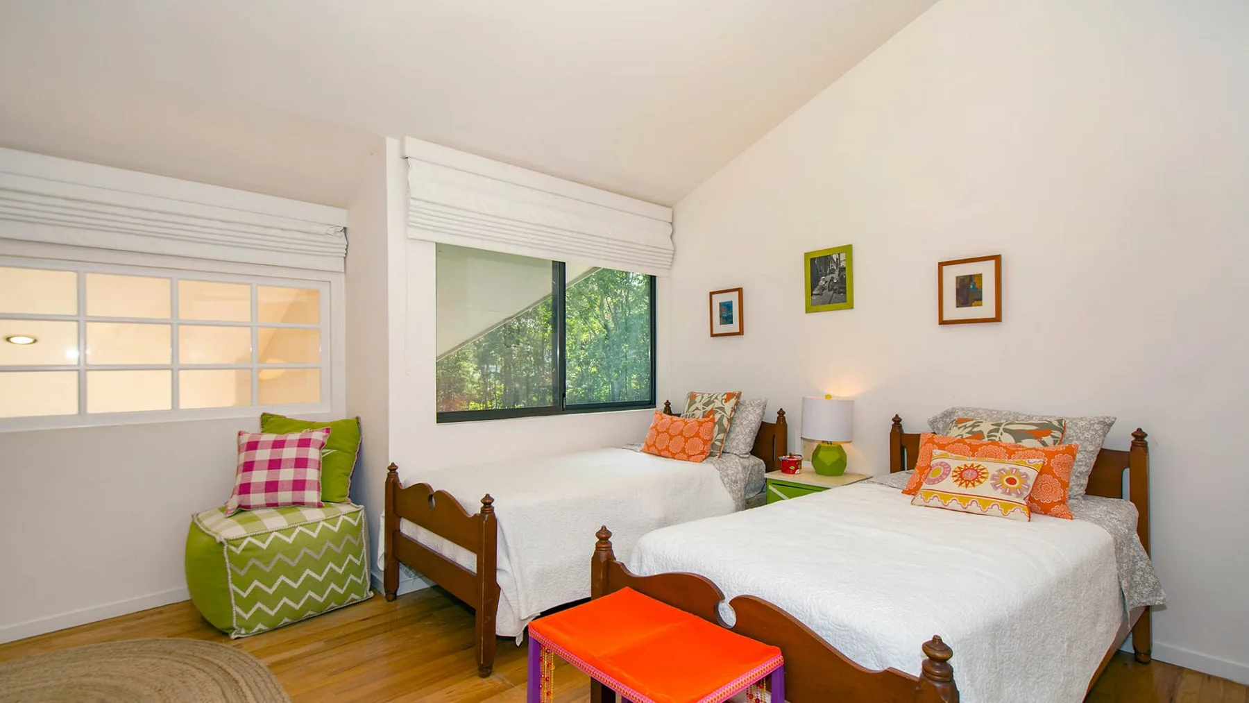 A bright bedroom with two beds and a green armchair by the window.