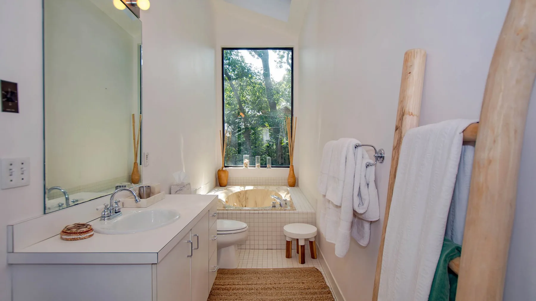 A bright bathroom with a sink, toilet, and bathtub beside a window.