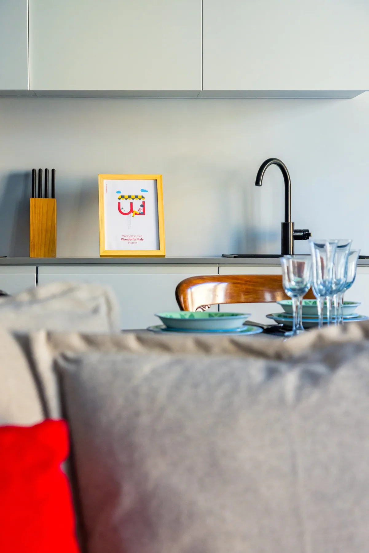 A dining table set with glassware sits in front of a compact kitchen.