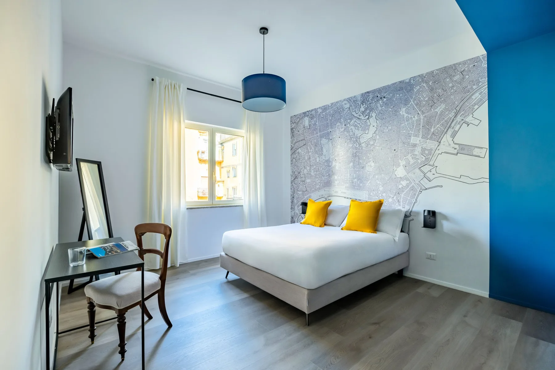 A bright bedroom with a white bed, yellow cushions, and a large wall mural.