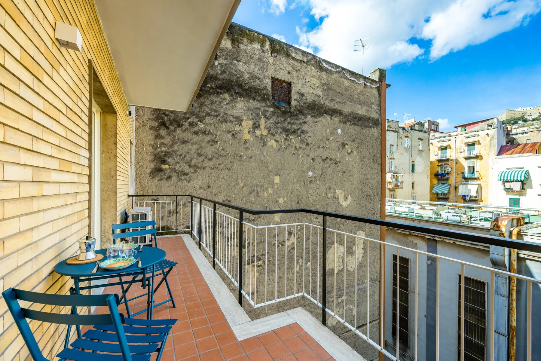 A small balcony with metal seating and a railing overlooks nearby buildings.
