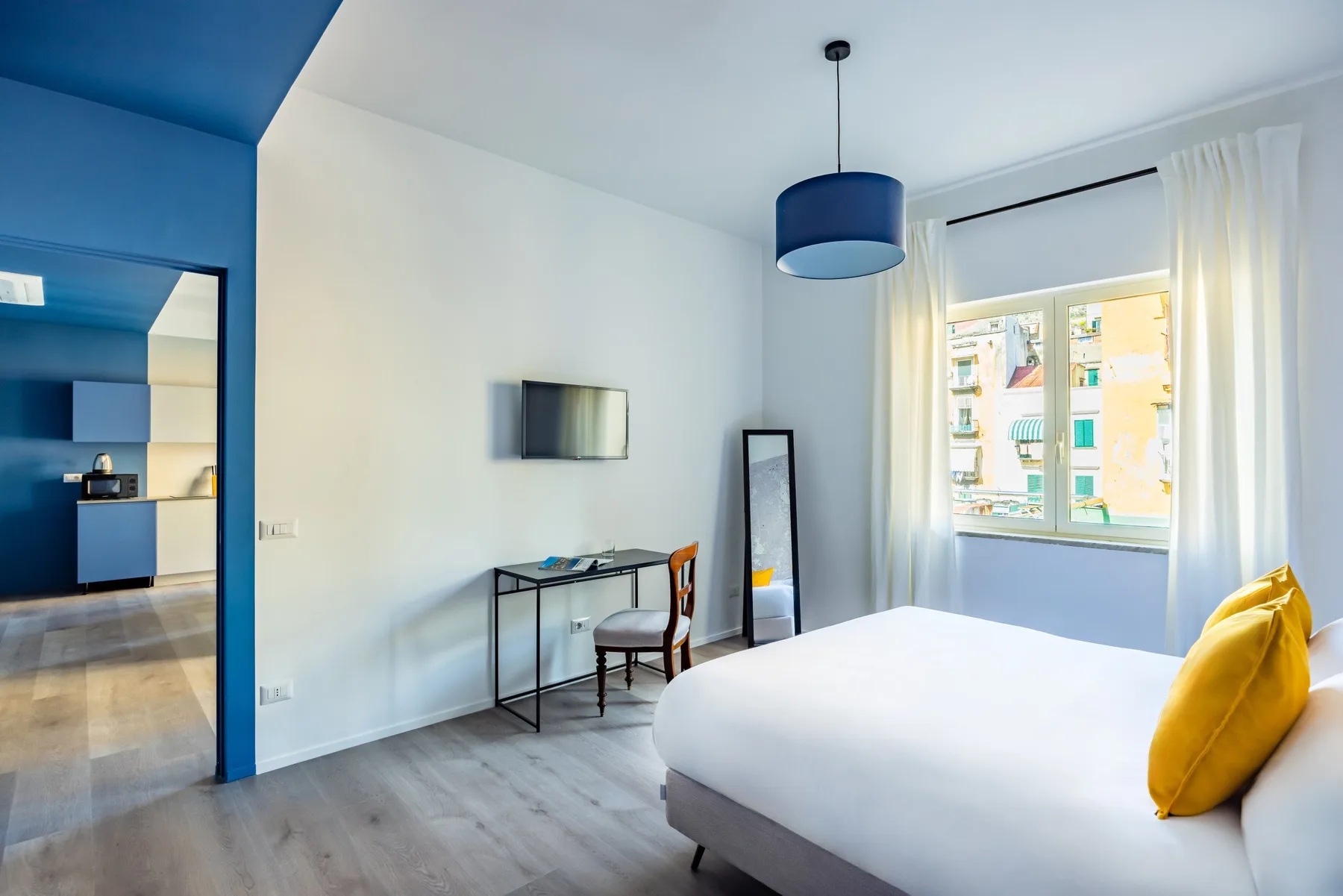 A bright bedroom with a bed, desk, and a window framed by curtains.