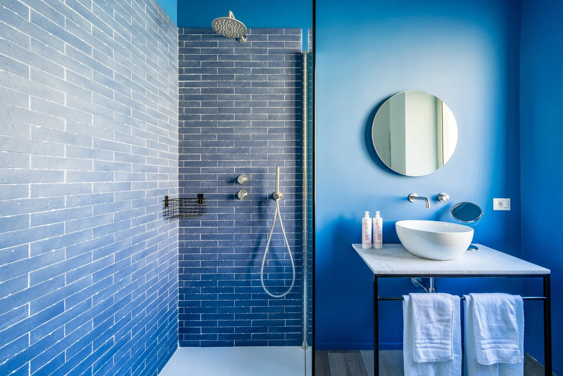A blue bathroom features a tiled shower and a sink beneath a round mirror.