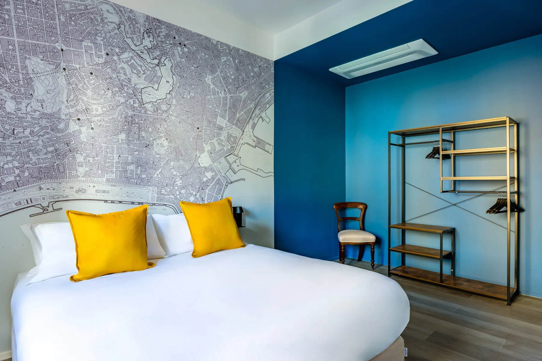 A bedroom with white bedding, yellow pillows, and a large wall map.