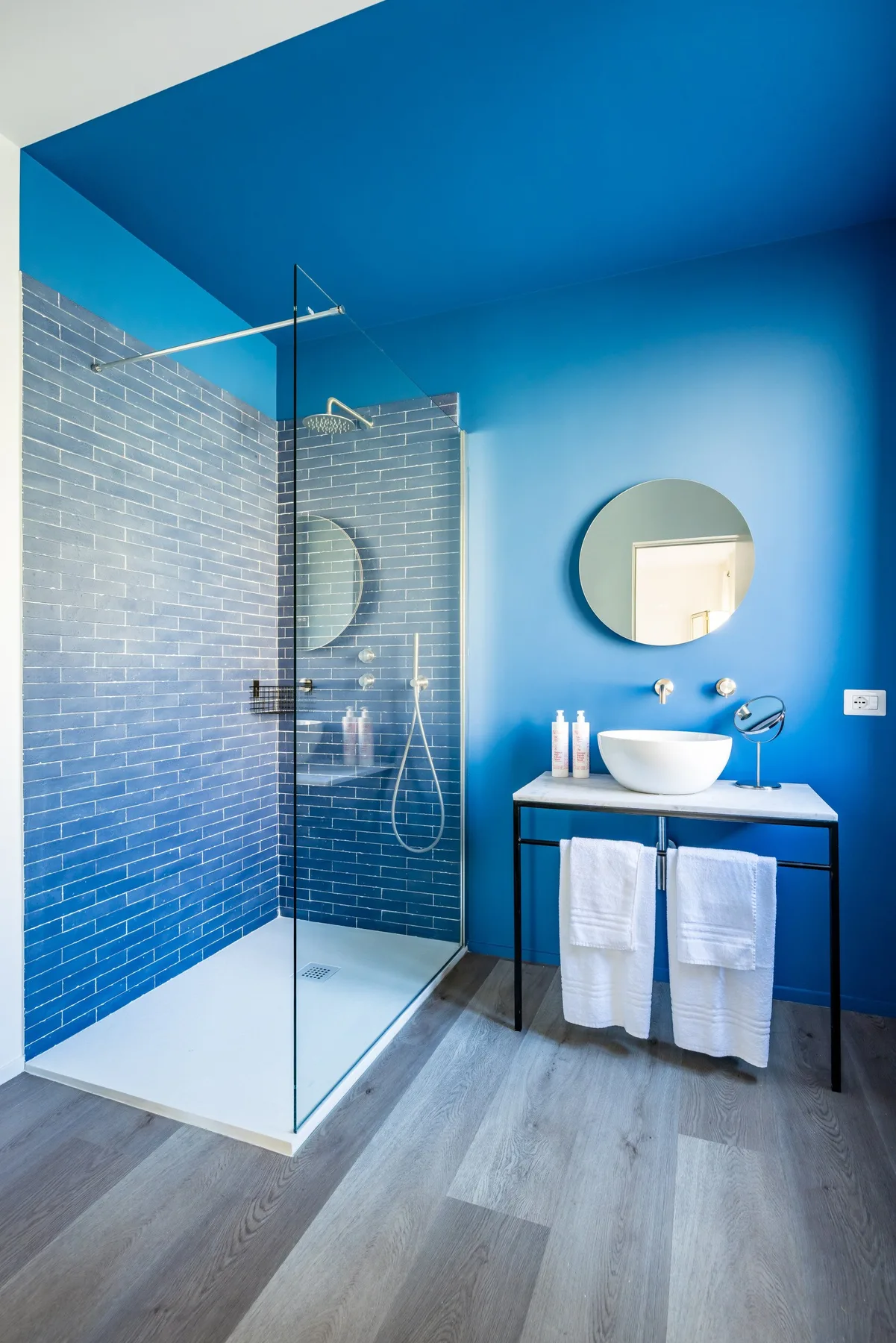 A bright bathroom with a glass shower, blue walls, and a sink vanity.