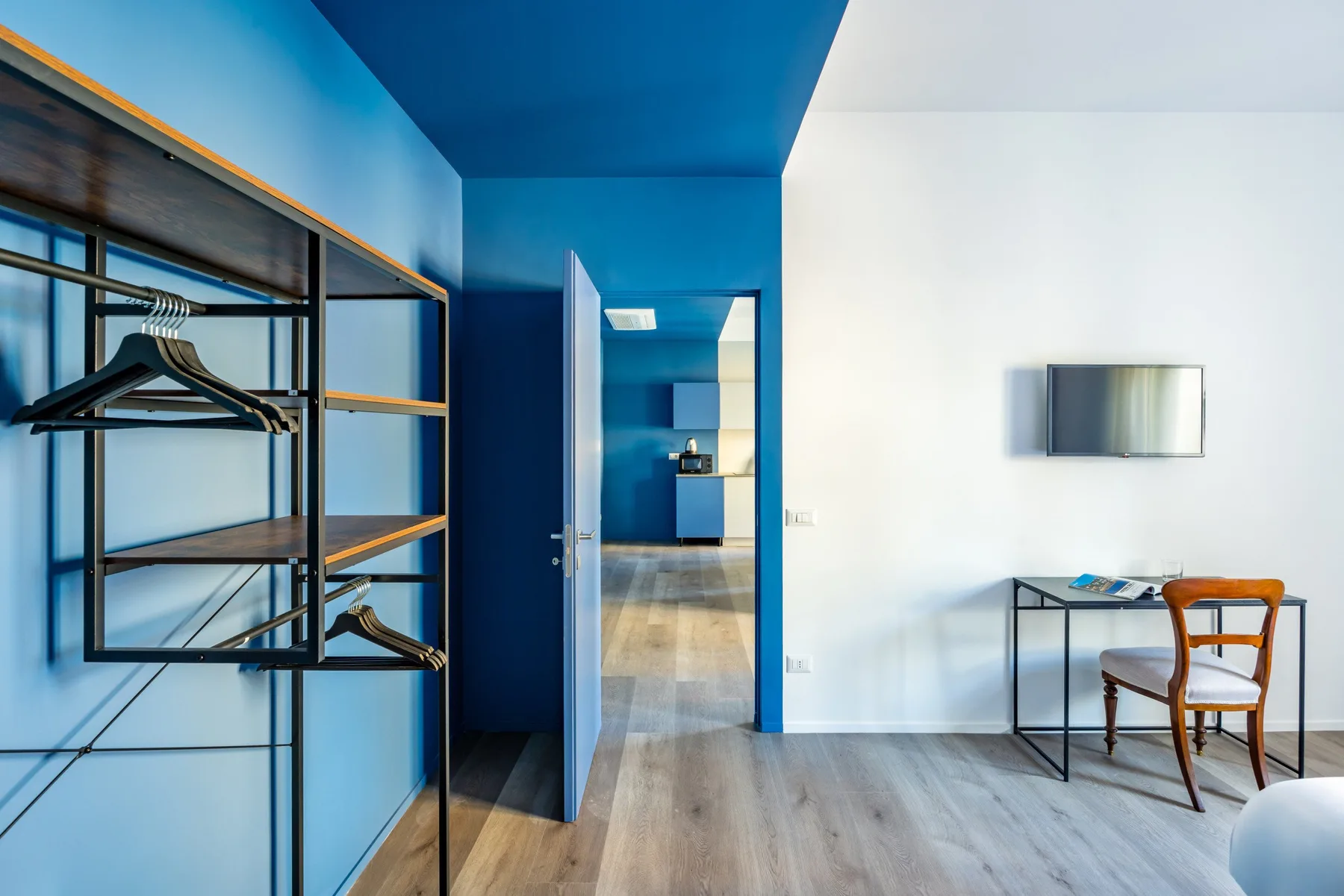 A bright room with open clothing racks, a small desk, and a doorway to a kitchen.