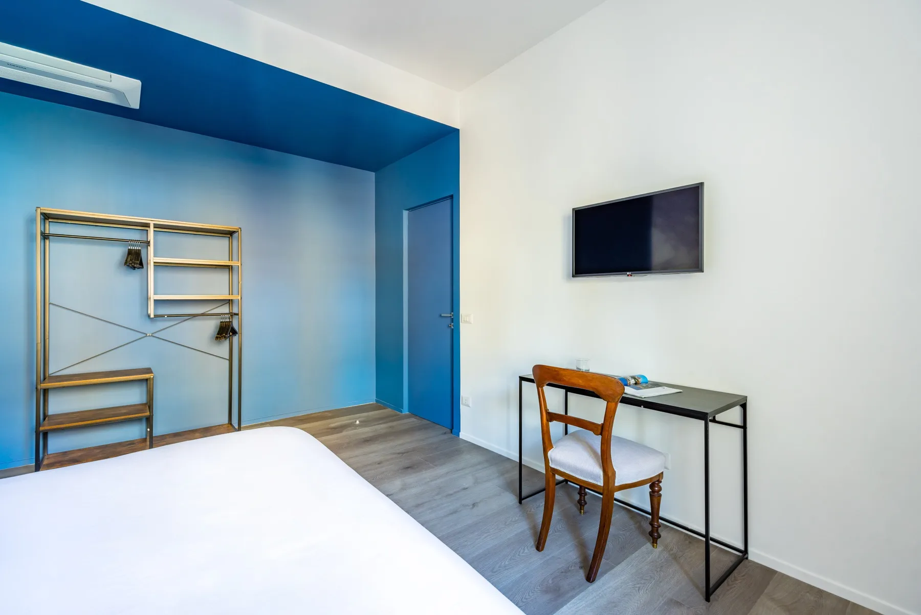 A bedroom with a bed, desk, chair, and wall-mounted television.