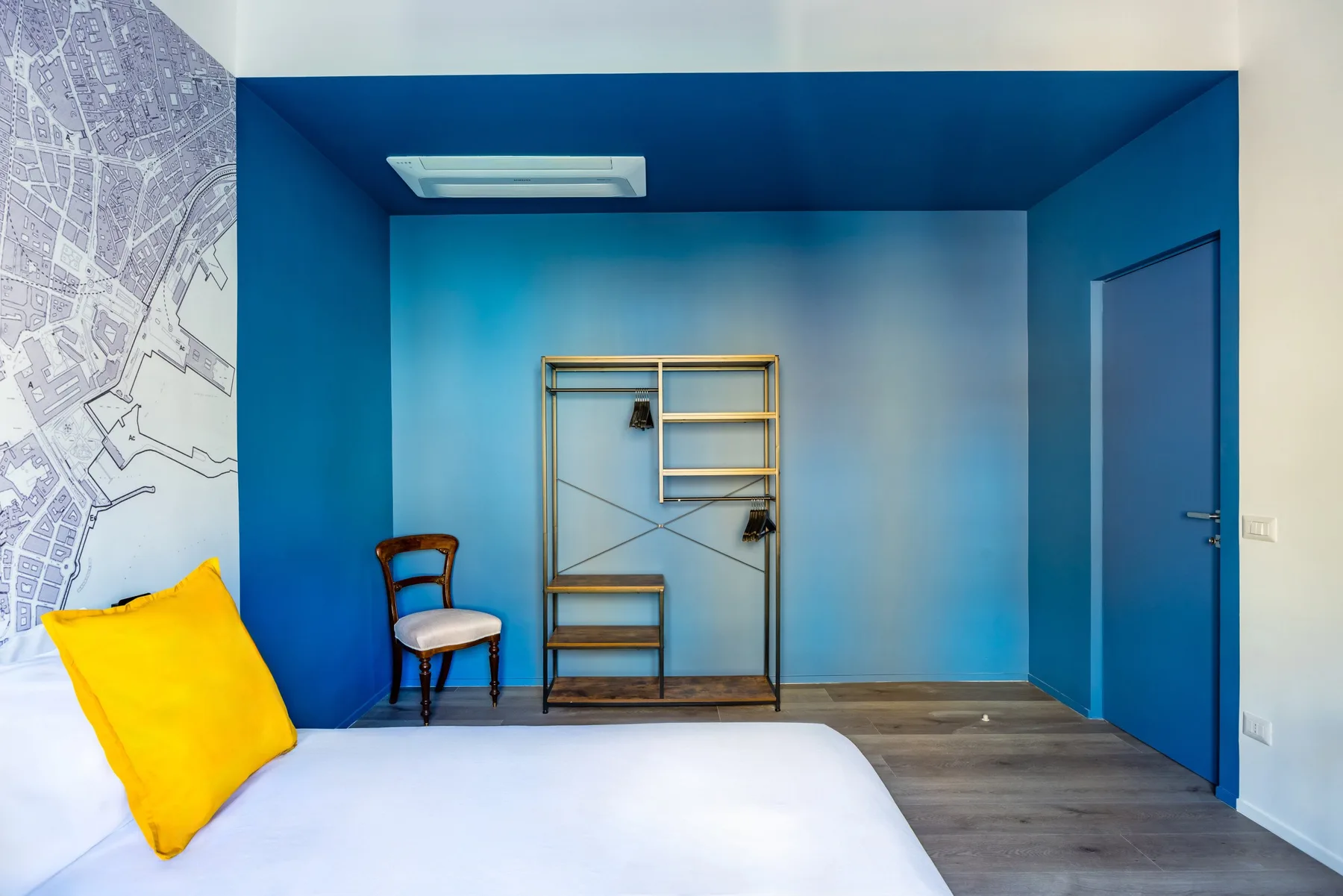 A bedroom with a bed, a chair, and open shelving against blue walls.