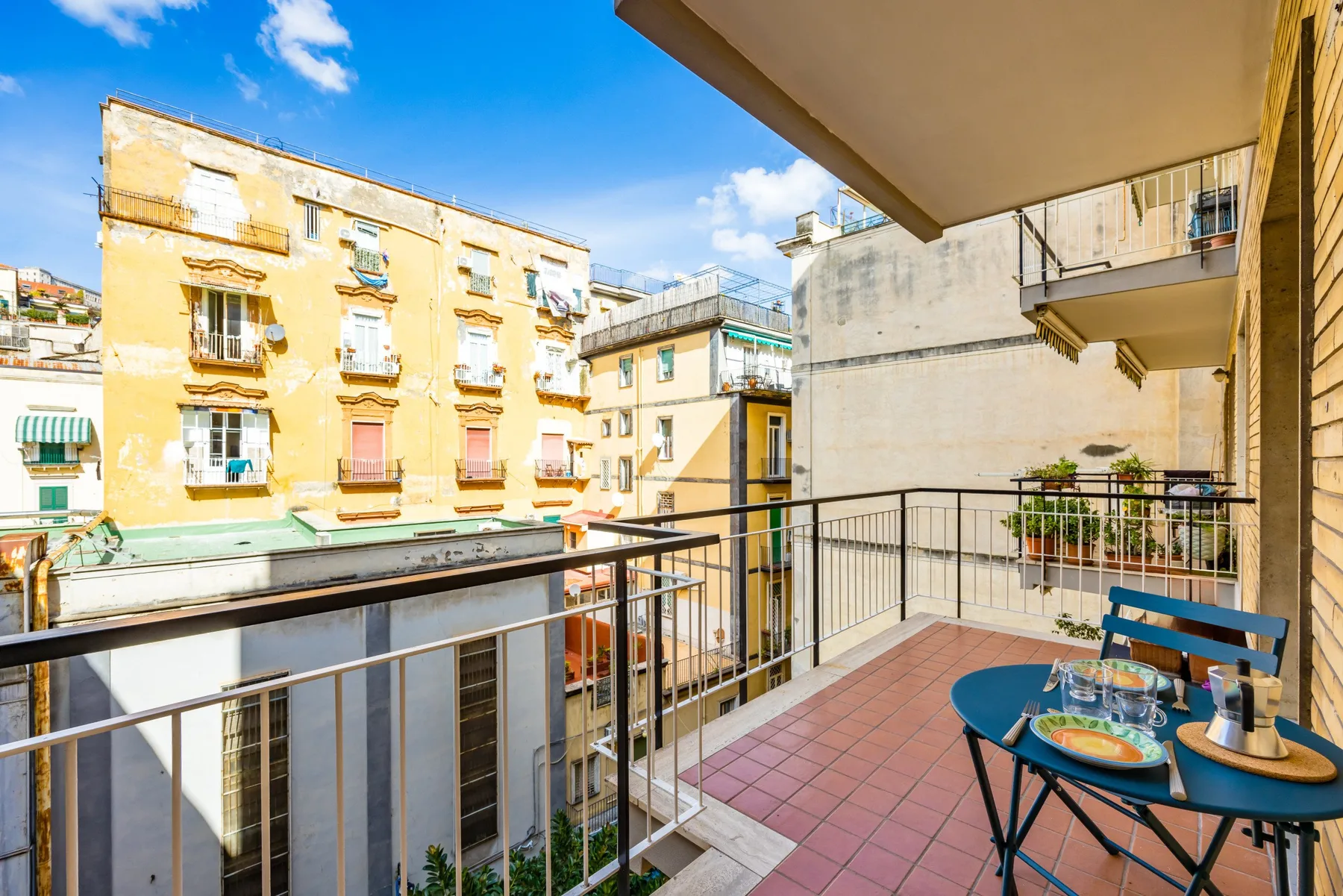 A balcony overlooks nearby apartment buildings, with a small table and chairs.