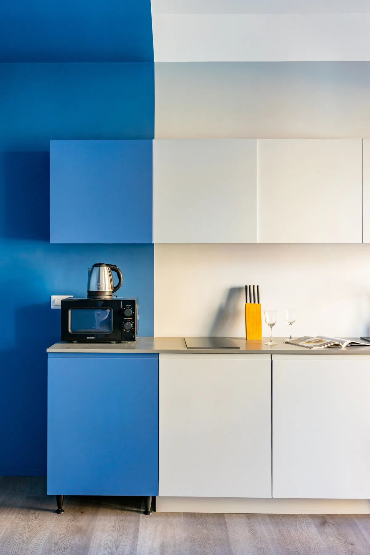 A modern kitchenette with blue and white cabinets, a microwave, and a kettle.