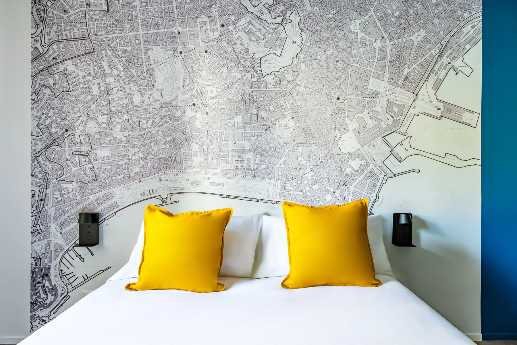 A bed with bright yellow pillows sits beneath a large wall map.