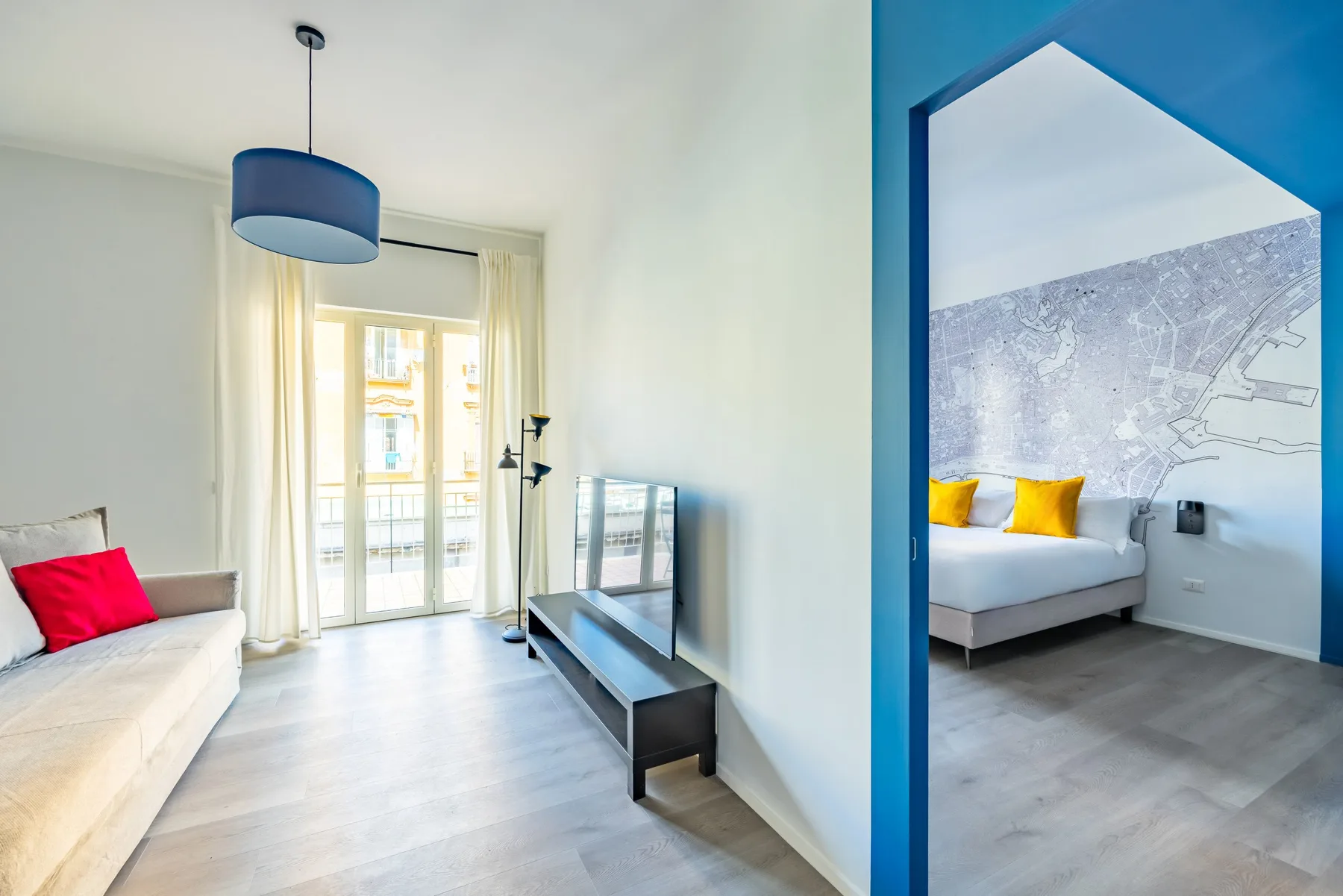 A bright living room with seating, a television, and a doorway to a bedroom.