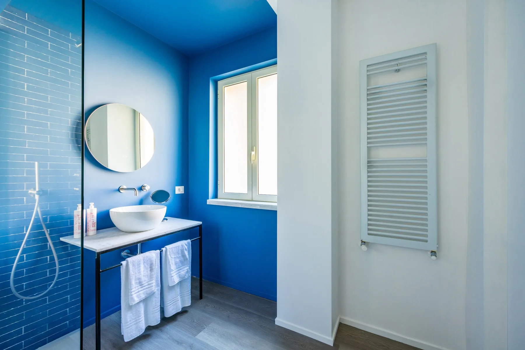 A bright blue bathroom with a vanity, basin, and window.