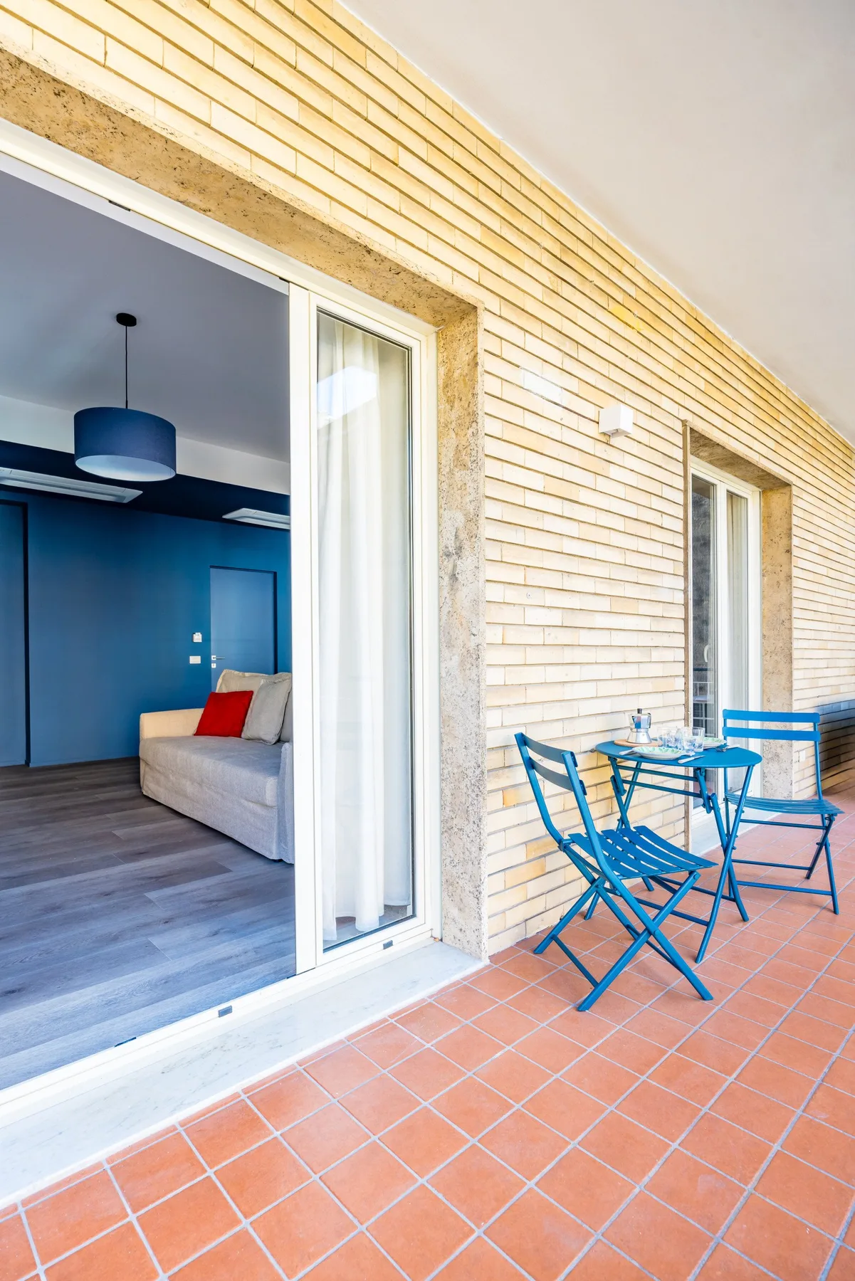 A tiled terrace with blue outdoor seating beside an open room.