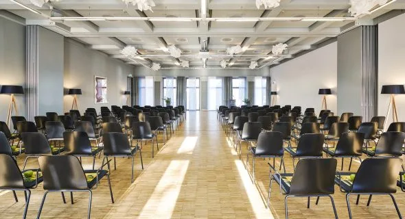 Sala de conferencias con filas de sillas y una zona para presentaciones.