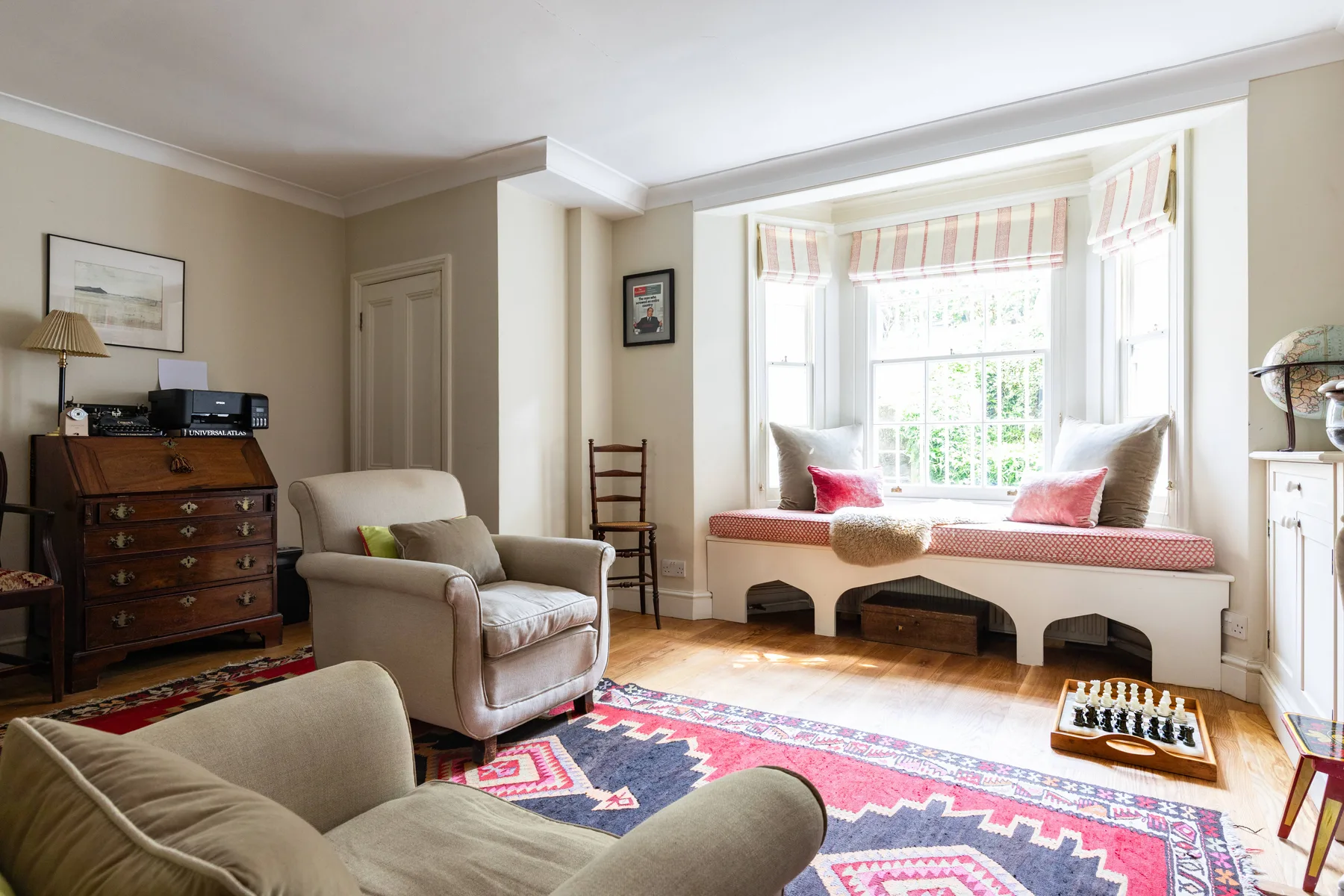 A bright living room with a window seat, armchairs, and a patterned rug.