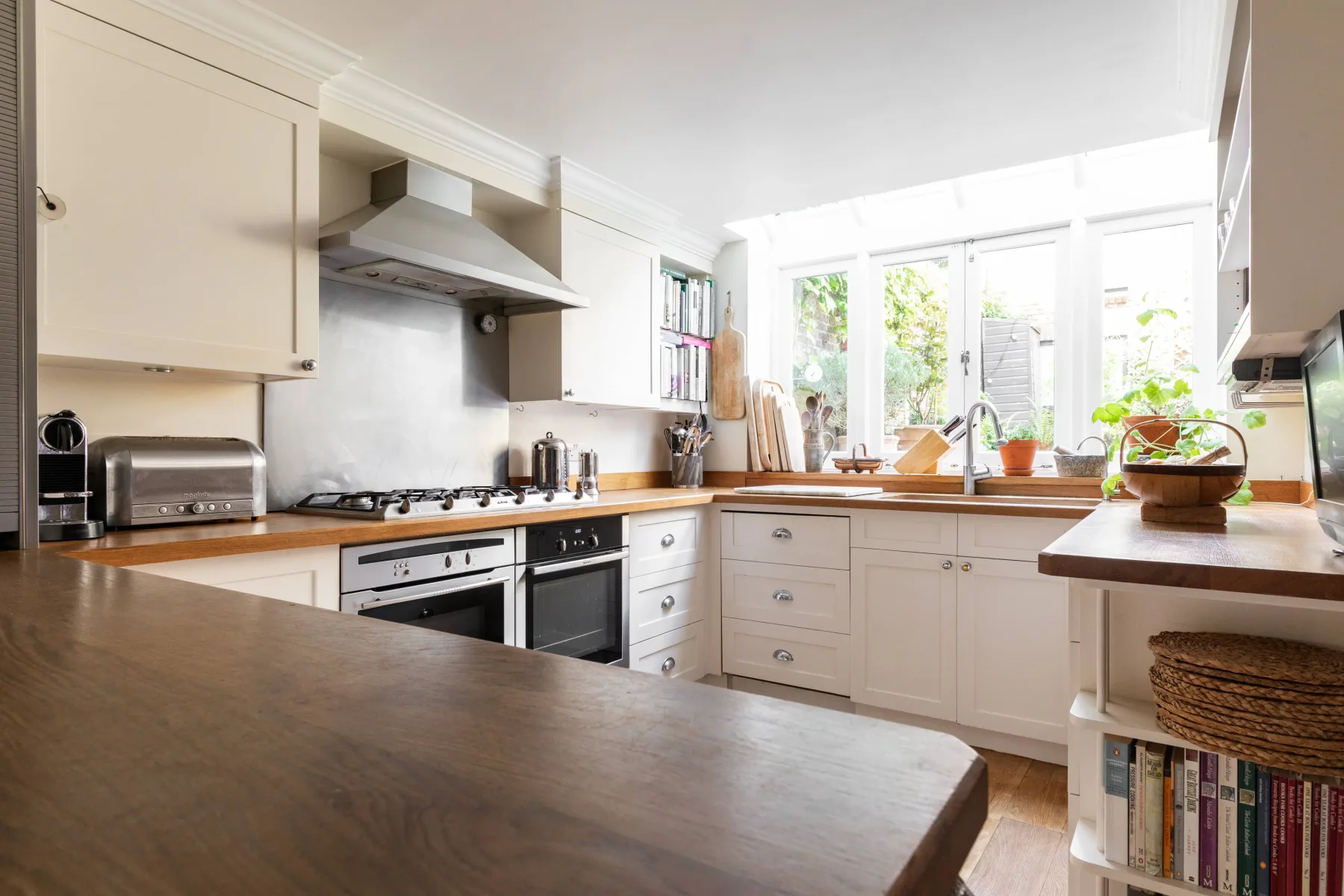A bright kitchen with white cabinetry, wooden countertops, and large windows.