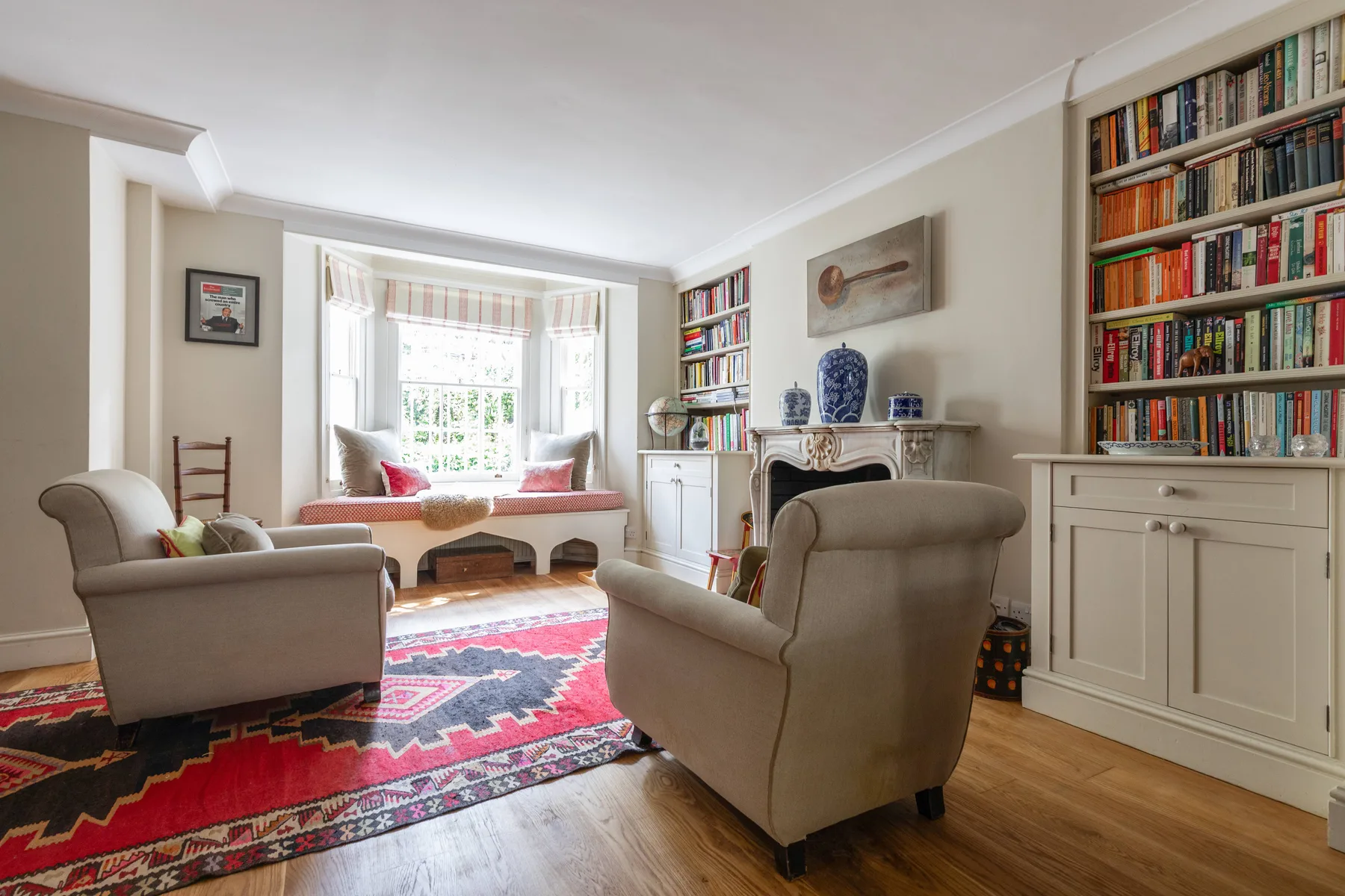 A bright living room with armchairs, built-in bookshelves, and a window seat.