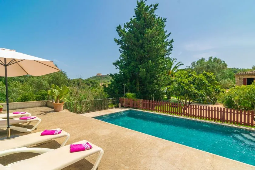 An outdoor swimming pool beside a paved deck with lounge seating and an umbrella.