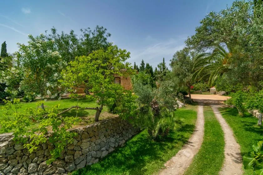 A garden path winds past leafy trees and a low stone wall.