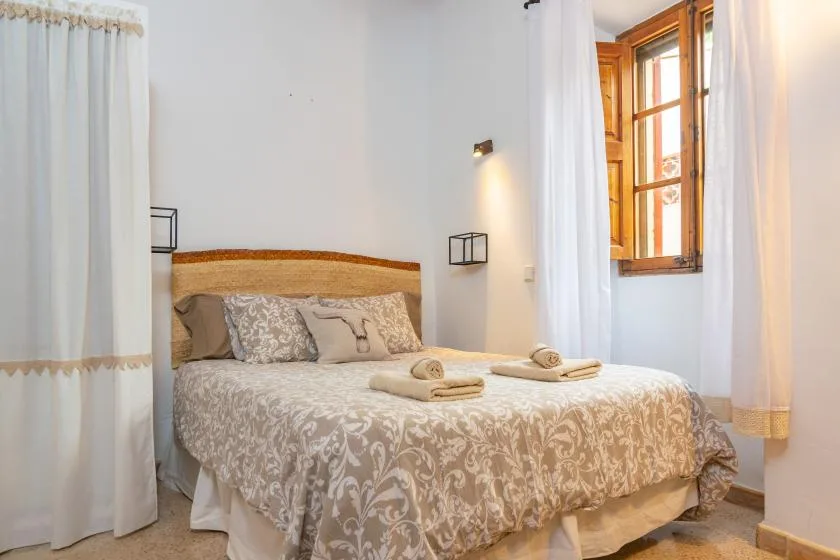 A bedroom with a bed dressed in patterned bedding beside a sunlit window.
